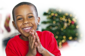 A young child in a red sweater with Christmas lights in the background.